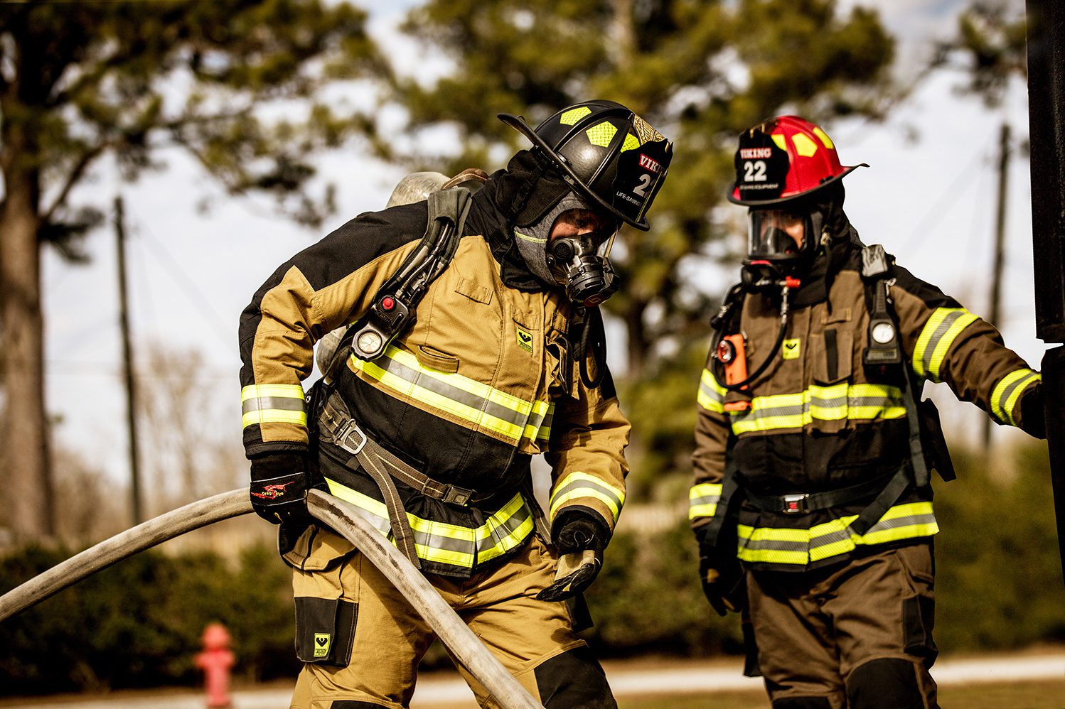 Two firemen in full gear are talking to each other.