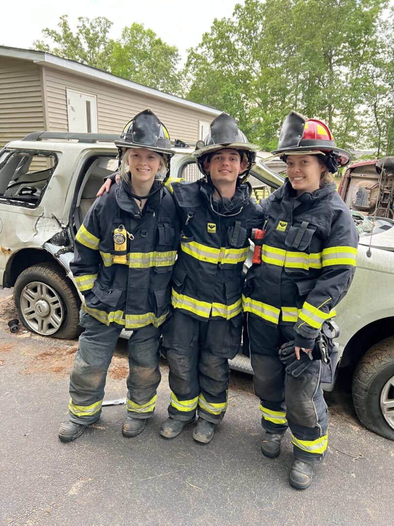 Three firefighters standing next to a car.