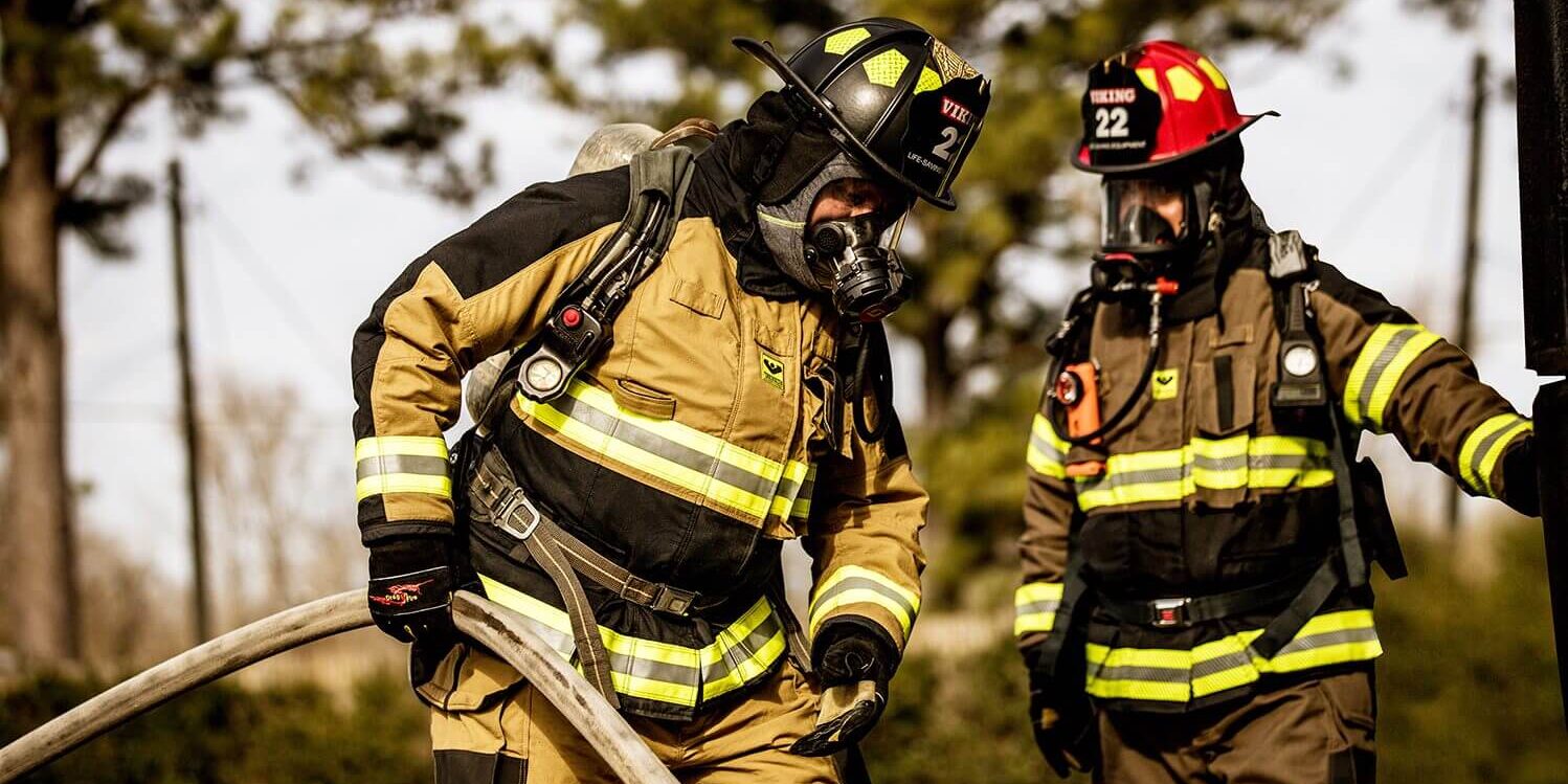 Two firemen in full gear are talking to each other.